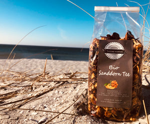 Bild zeigt Bio Sanddorn Tee von Thieme Kontor. 100 Gramm Packung. Am Strand von Zingst. Im Hintergrund ist die Ostsee.